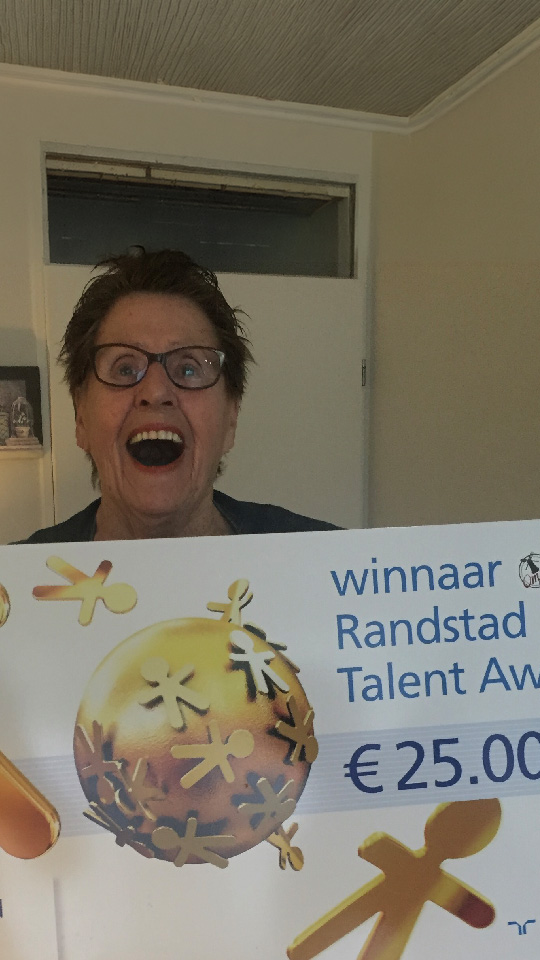 An elderly woman celebrating with the winner's cheque for the Randstad Talent Award